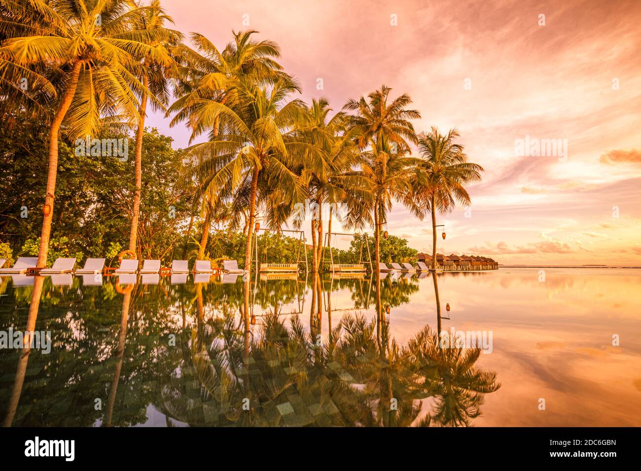 Palmen Stühle rund um Infinity-Pool in der Nähe Meer Ozean Strand bei Sonnenaufgang oder Sonnenuntergang Zeit. Für Urlaubsreisen und Urlaubskonzept, Sommerresort Stockfoto