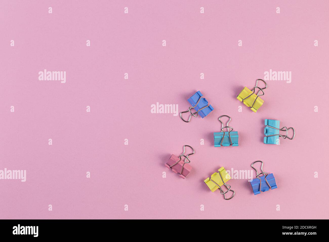 Farbiges Eisen Büroklammern auf einem rosa Hintergrund, Binder Clip ist ein einfaches Gerät zum Binden von Papier zusammen, Metallklammern im Chaos. Office suppl Stockfoto