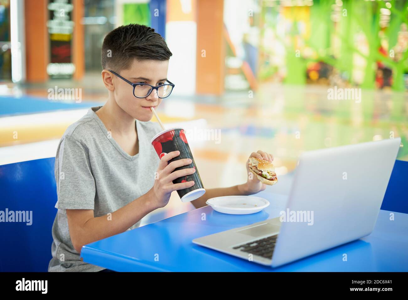 Teenager essen ungesunde Fast Food und trinken Soda während des Sitzens Am Laptop in einem Food Court Stockfoto