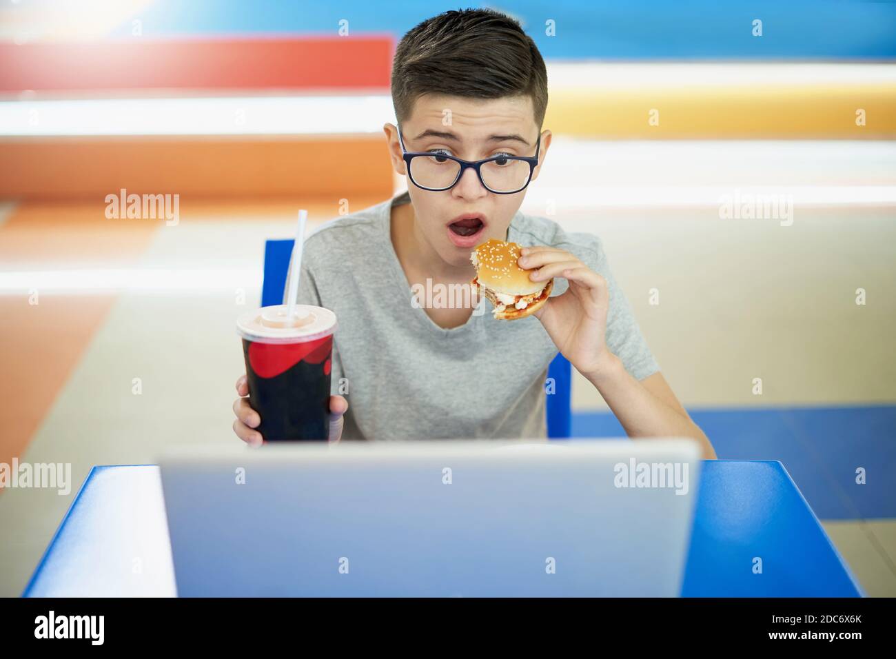 Kaukasischen weißen Teenager essen Burger und schauen überrascht Laptop Stockfoto