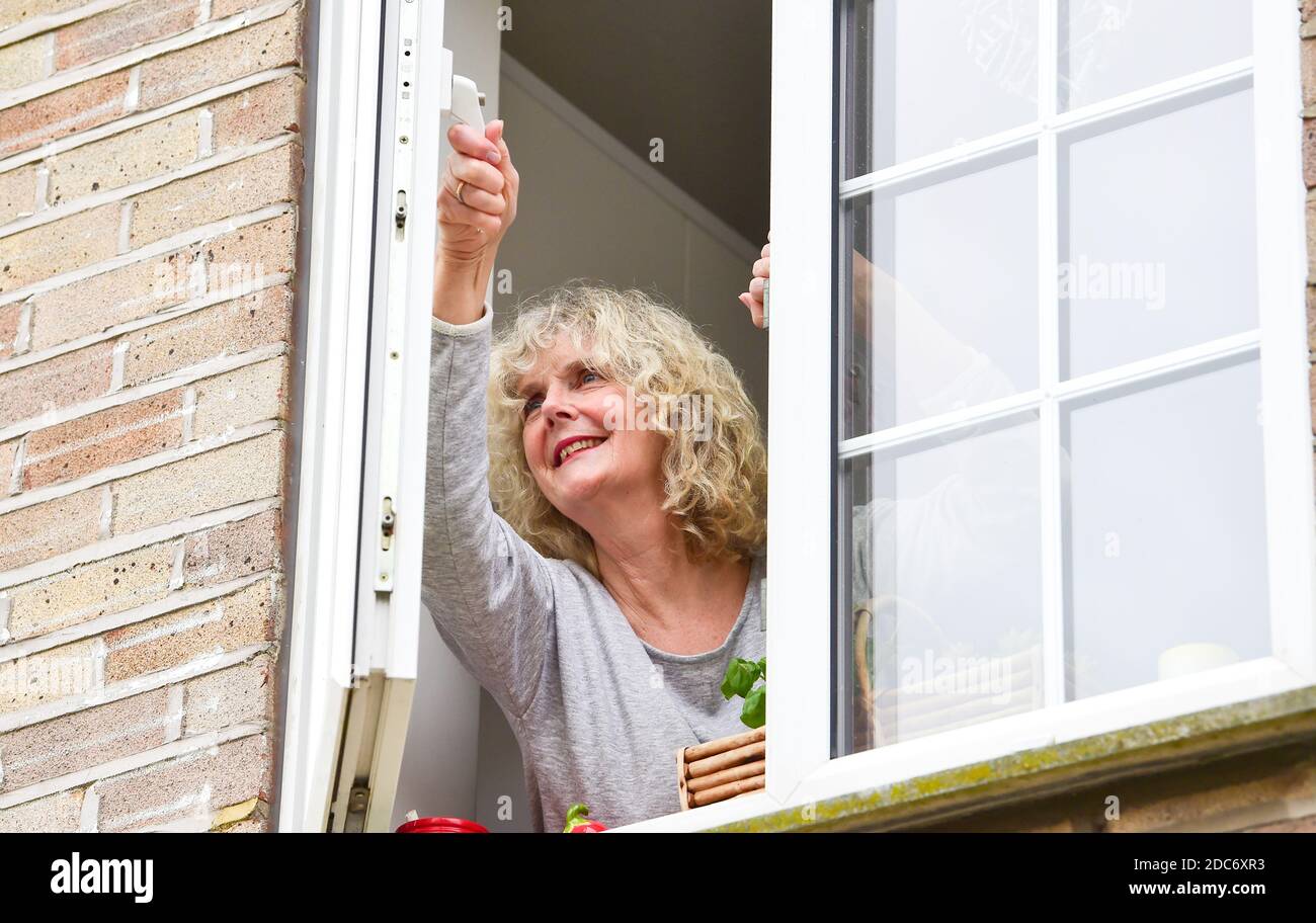 Frau zu Hause öffnet Küchenfenster, um frisch einzulassen Luft wie empfohlen, um zu helfen, Coronavirus COVID-19-Virus zu bekämpfen Stockfoto