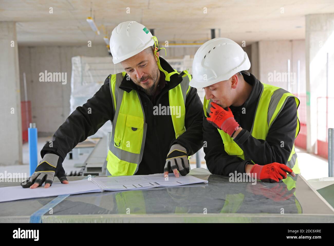 Zwei männliche Bauingenieure diskutieren Zeichnungen auf einer großen Londoner Baustelle. Stockfoto