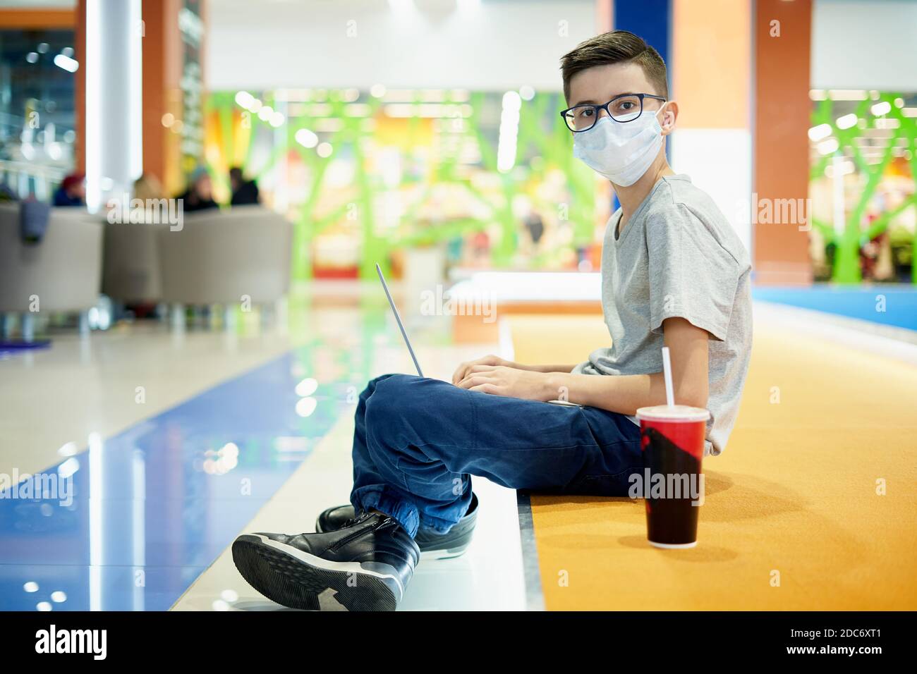 Porträt eines Teenagers in einer Schutzmaske mit Ein Laptop in einem Einkaufszentrum Stockfoto