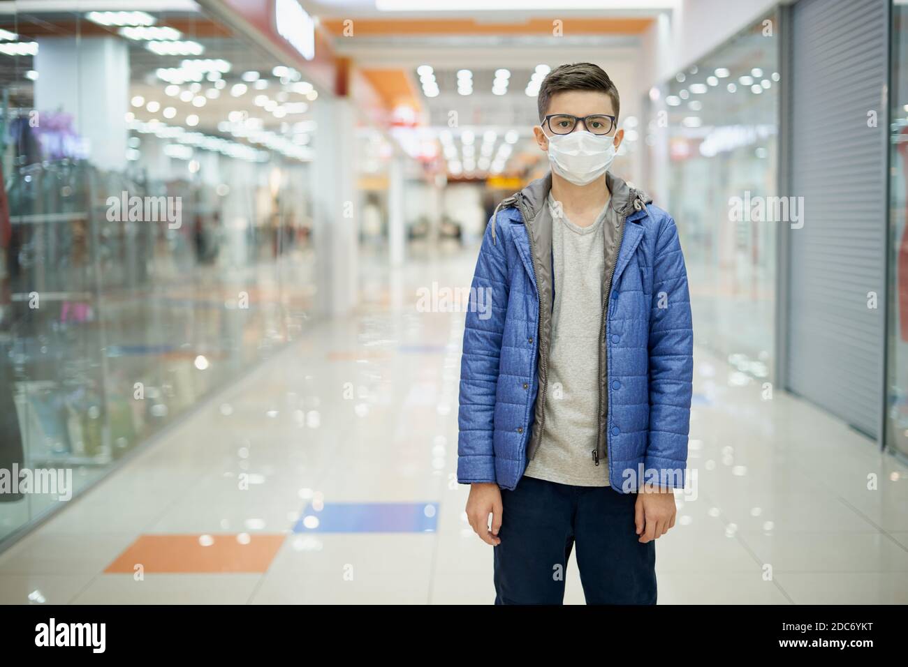 Porträt von einsamen schweren Teenager-Jungen in Schutzmaske in Leeres Einkaufszentrum Stockfoto