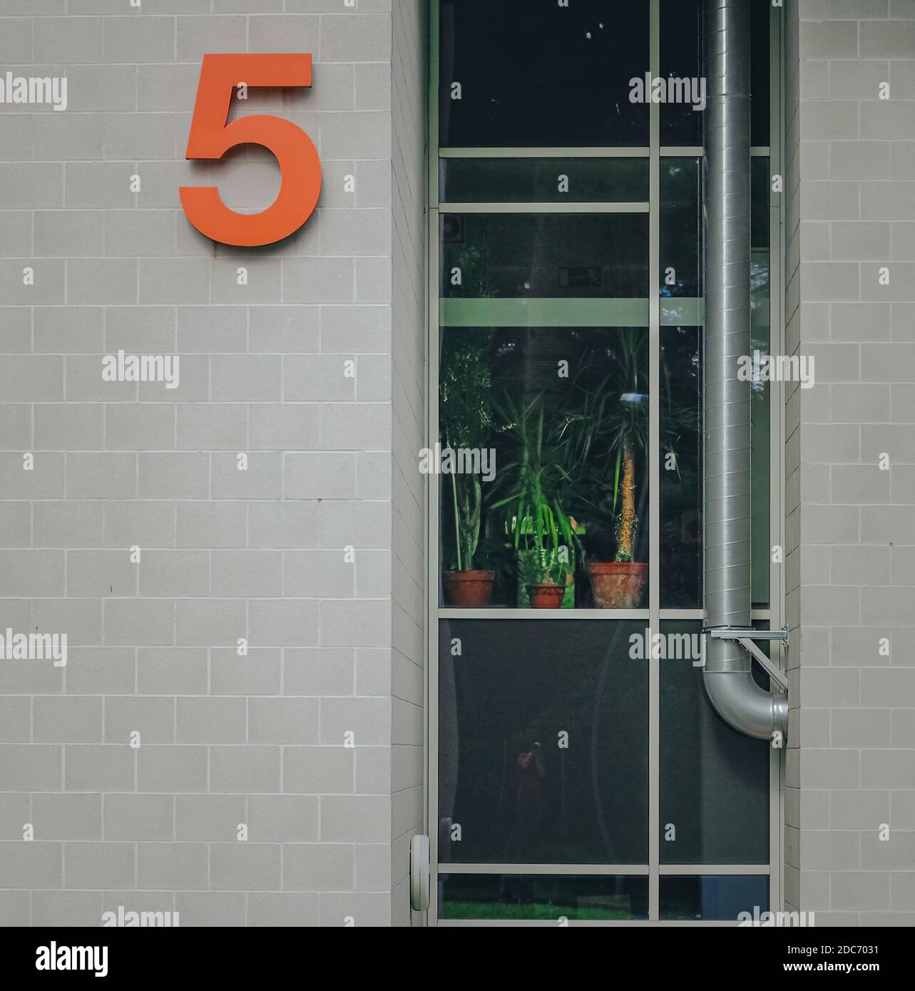 Orange Haus Nummer 5 an der Außenfassade einer modernen Architektur mit Klinkerziegel Wand und Bodenverglasung. Orangene Hausnummer 5 an der Außenfassade Stockfoto