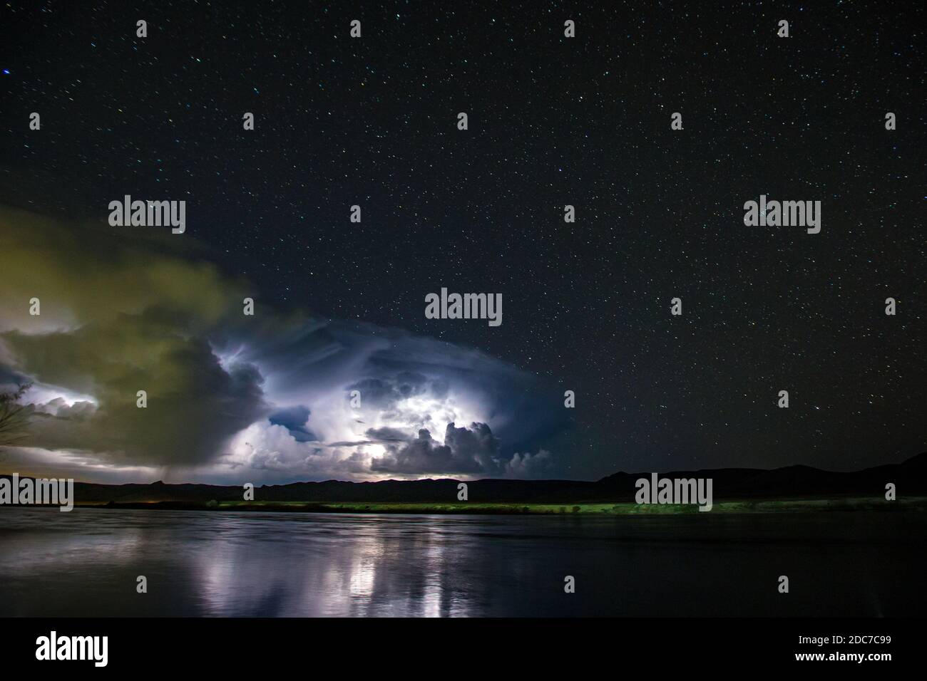 Zahlreiche Blitze beleuchten nachts große Wolken. Sternenklare Nacht am Flussufer vor einem Gewitter. Stockfoto