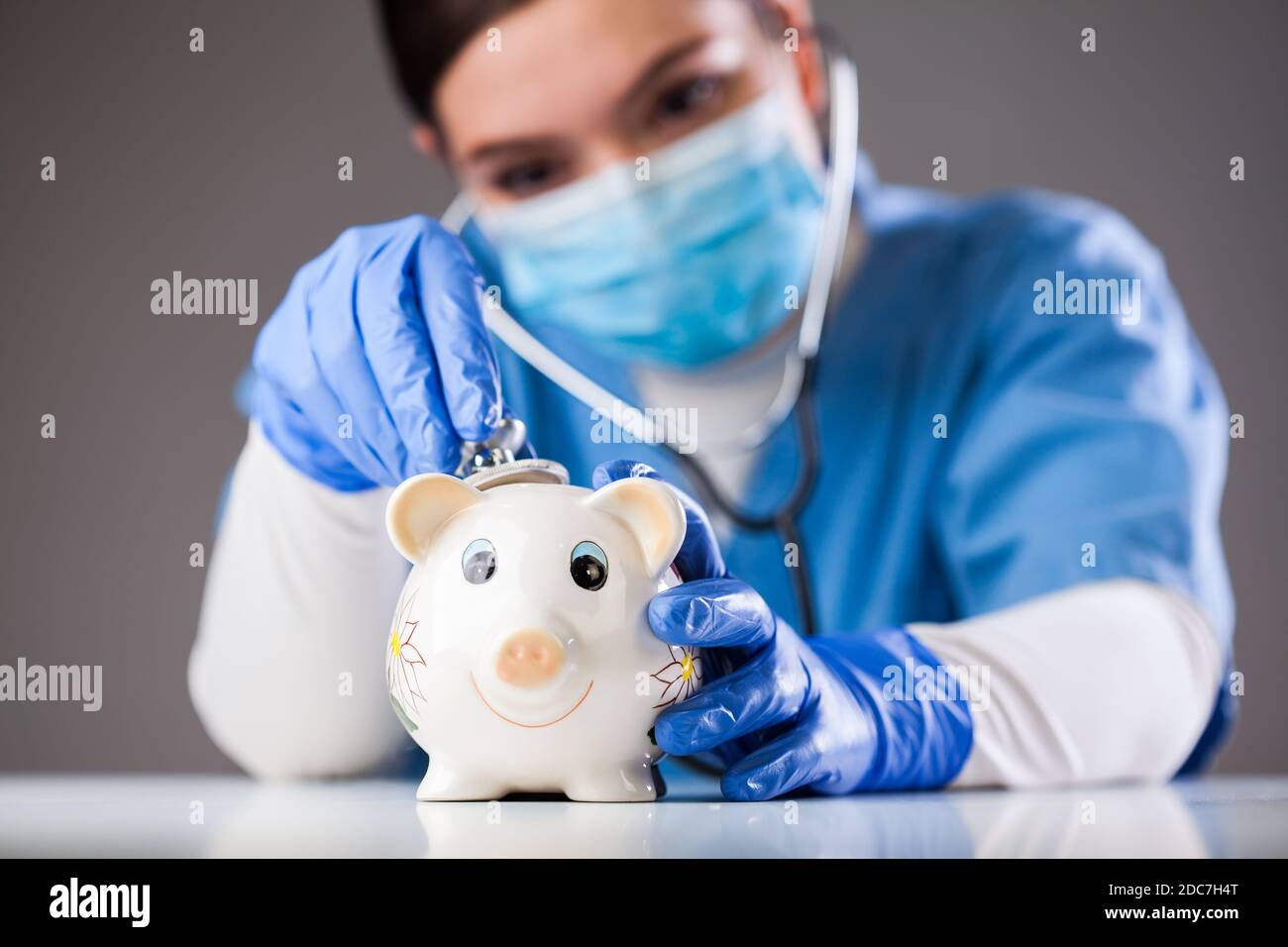 Arzt inspiziert Sparschwein mit Stethoskop, Wirtschaft Rezession aufgrund der globalen COVID-19 Coronavirus Welt Pandemie Ausbruch, finanzielle Härte Stockfoto