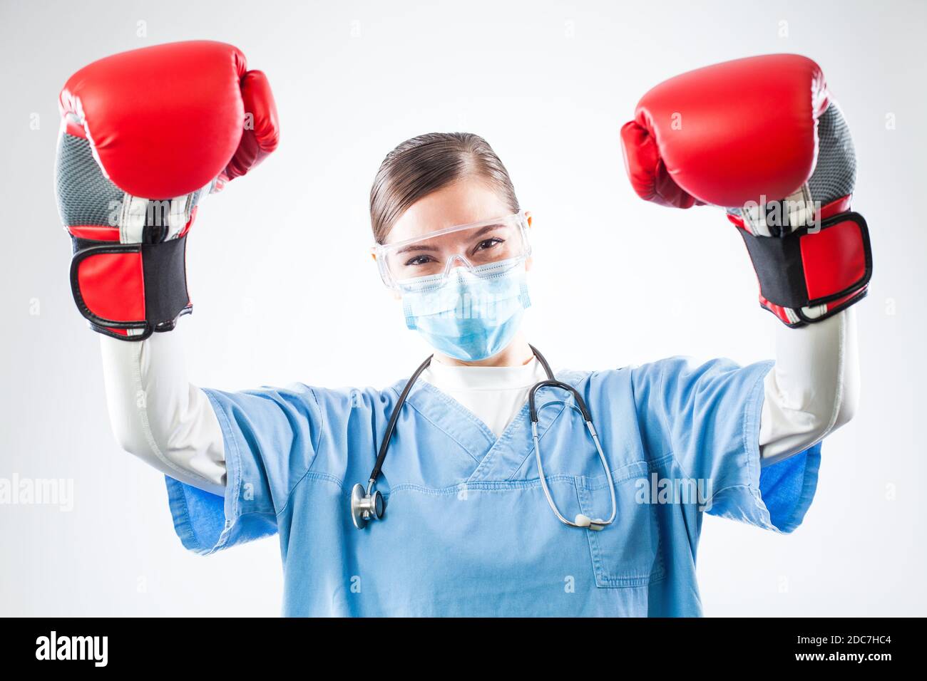 Siegreiche junge kaukasische Ärztin mit blauen Uniform roten Boxhandschuhen, in der Luft erhobene Hände, zufrieden und glücklich nach dem Überleben des Patienten Stockfoto