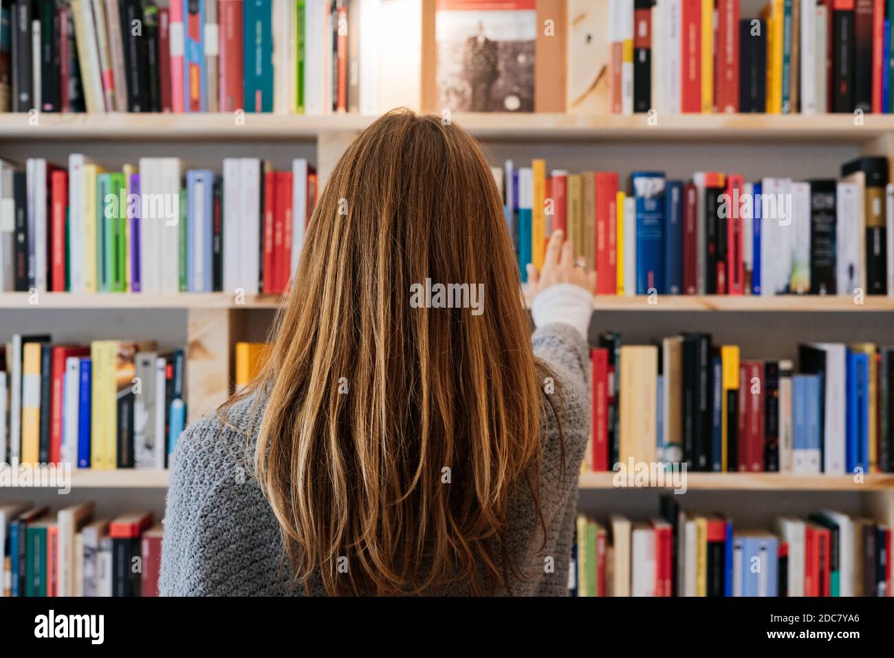 Junge blonde Frau auf dem Rücken Wahl eines Buches in einer Buchhandlung. Stockfoto