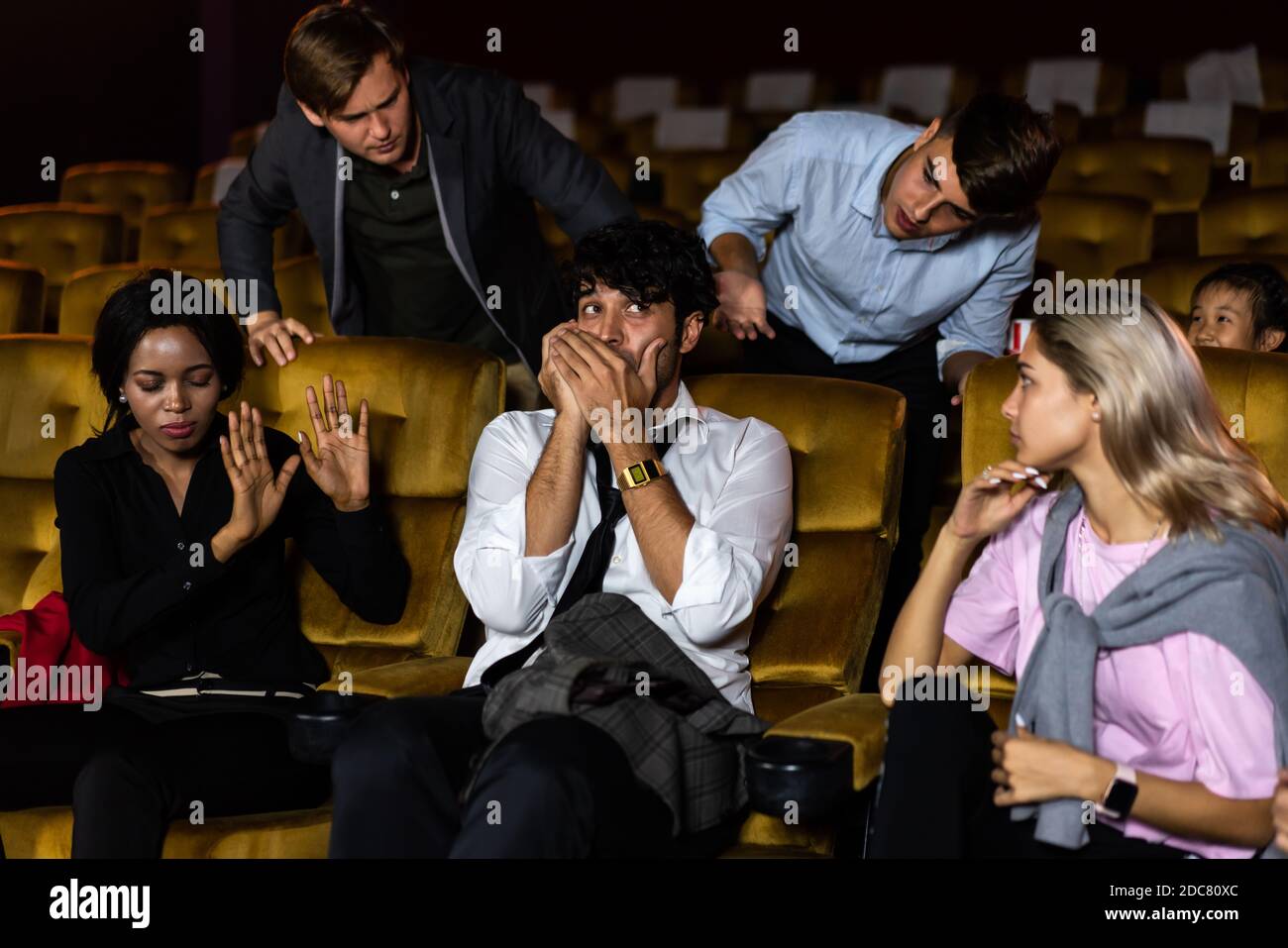 Ärgerlicher Mann, der auf dem Handy am Kinosaal mit Menschen im Kino spricht, ist wütend auf ihn Stockfoto
