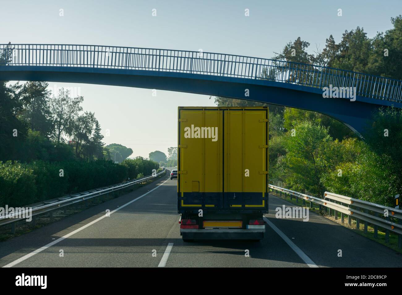 Anhänger mit geschlossener Box und gelber Farbe fahren auf einer Autobahn und unter einer Fußgängerbrücke. Stockfoto