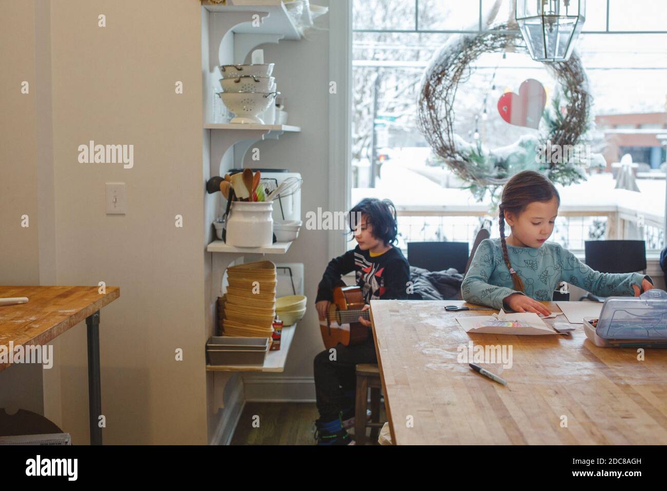 Zwei Kinder sitzen zusammen in der Küche und schaffen Musik und Kunst Nach Fenster Stockfoto