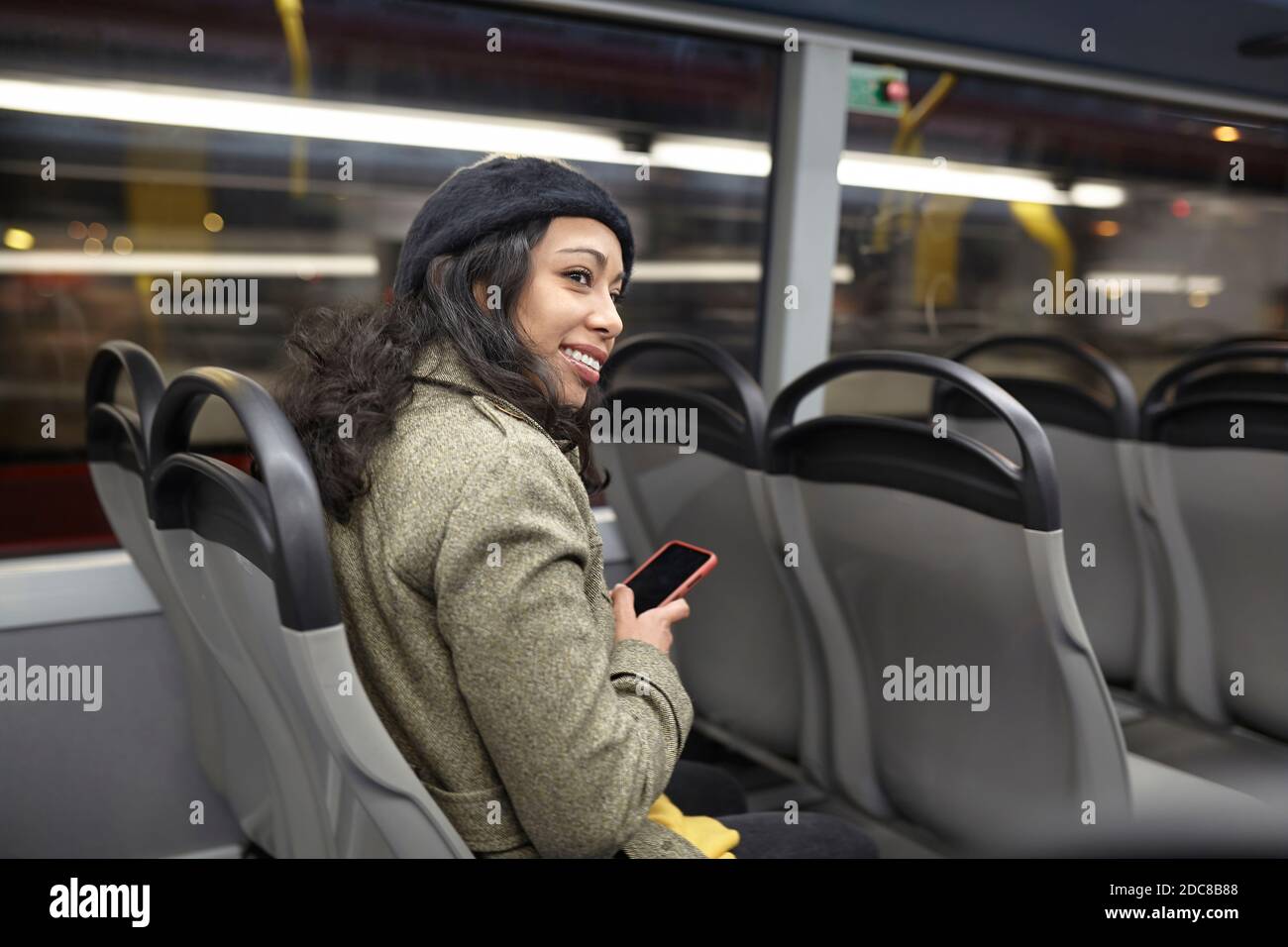 Lächelnde Frau sitzt in einem öffentlichen Bus in der Nacht Stockfoto