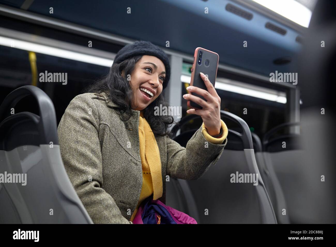 Lächelnde Frau, die in der Öffentlichkeit sitzt und sein Handy benutzt Bus bei Nacht Stockfoto