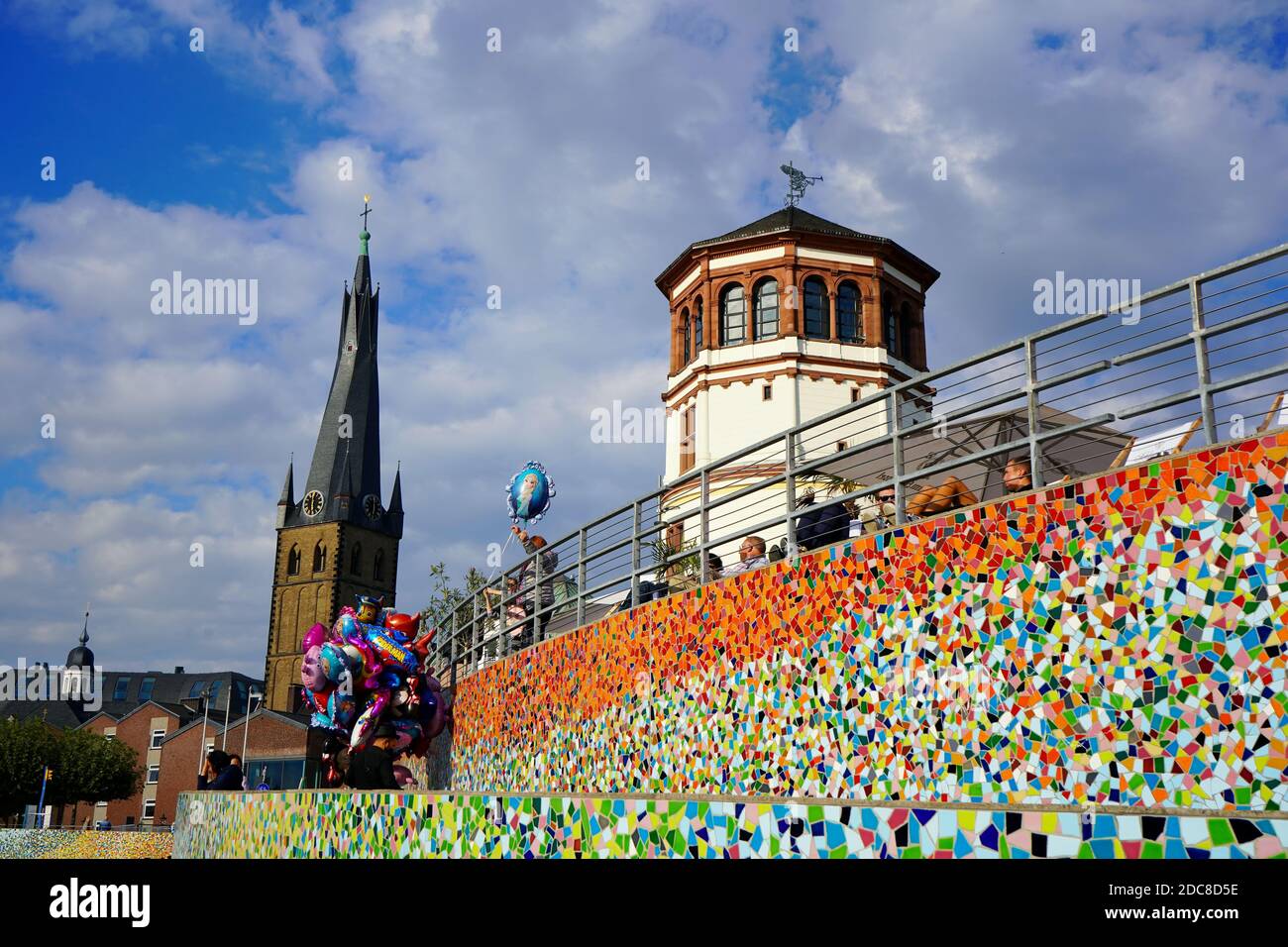 'Schlossturm' am Burgplatz mit dem bunten Mosaikkunstwerk 'Rivertime' von Hermann-Josef Kuhna und der Lambertus-Kirche im Hintergrund. Stockfoto