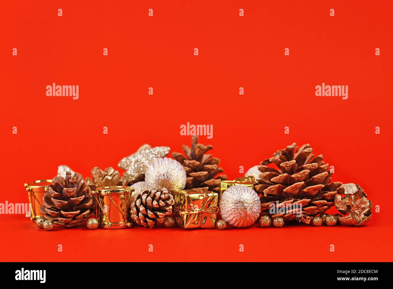 Weihnachtsarrangement mit goldenen Baumkugeln, Geschenkschachteln und Tannenzapfen auf hellrotem Hintergrund mit leerem Kopierraum Stockfoto