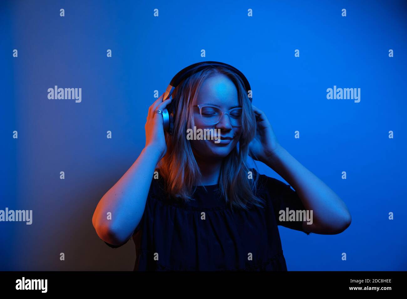 Junge kaukasische Mädchen mit Brille und Kopfhörer genießt die Musik auf einem hellen Neon-Hintergrund. Emotionen Konzept. Stockfoto