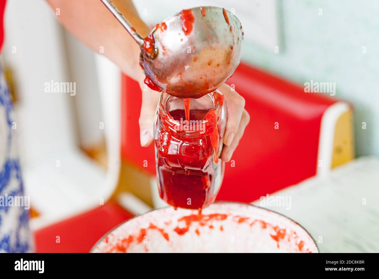 Gießen Sie frische Erdbeermarmelade in ein Glas mit Stahlpfanne Stockfoto