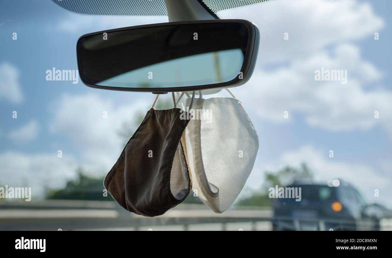 Zwei Schutzmaske hängen von te Rückspiegel eines Autos. Selektiver Fokus. Verschwommener Hintergrund. Stockfoto