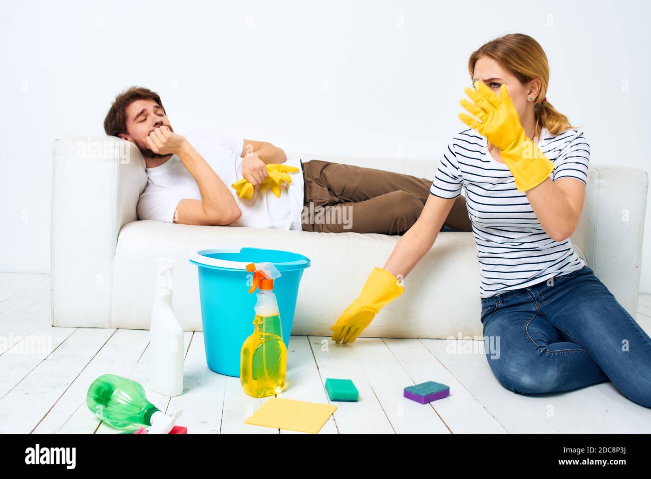 Ein Mann liegt auf einem Sofa. Eine Frau reinigt die Haushaltsreinigung Stockfoto