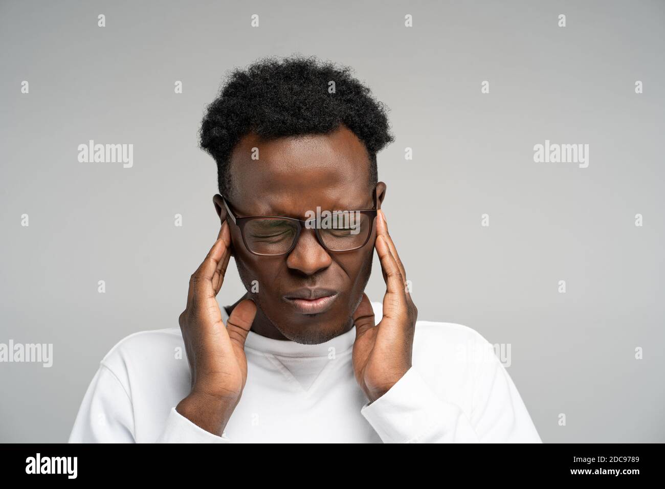 Afro Mann Gefühl Kopfschmerzen oder Migräne, massierenden Schläfen, erschöpft von Überlastung über grauen Hintergrund. Überfordert Mitarbeiter in Brillen leiden Stockfoto