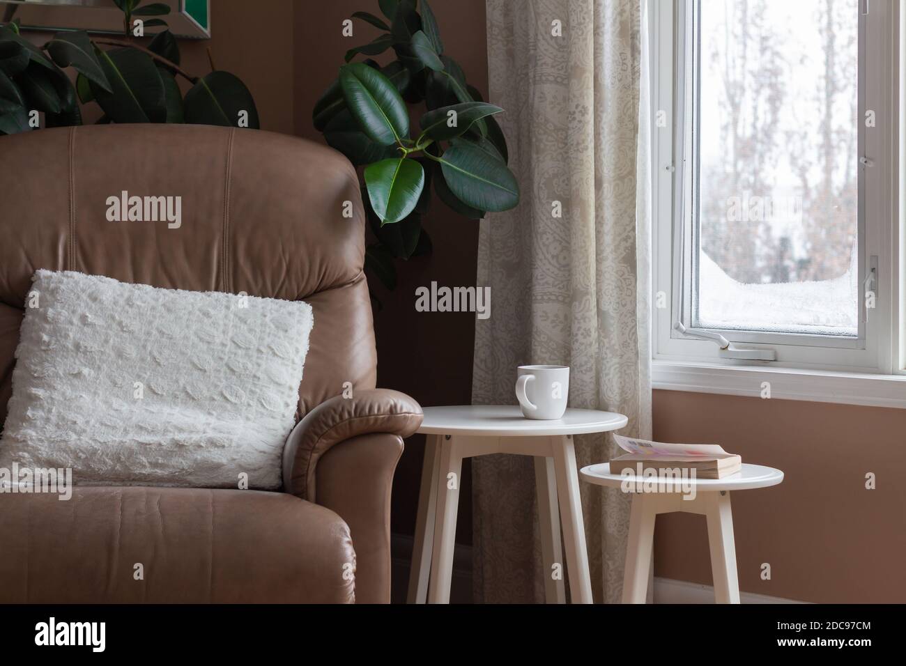 Indoor-Raum, gemütliche Ecke für Reflexion, Schnee Winter Szene aus dem Fenster, Kaffee und Buch auf Tischen mit Stuhl Stockfoto