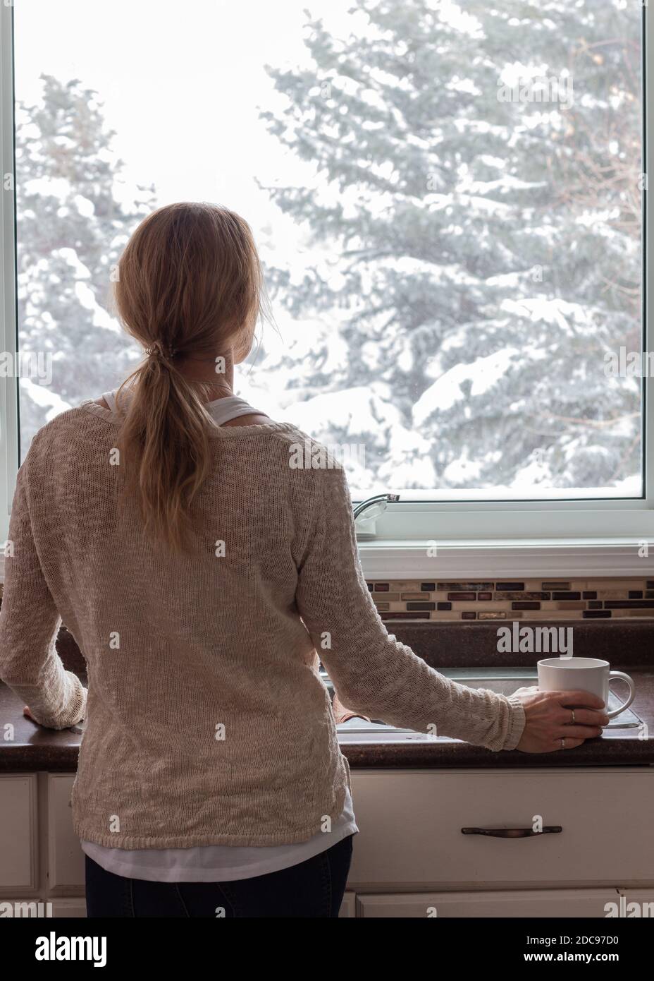 Portrait der Mutterschaft, Frau, die aus dem Fenster in der Küche mit Kaffee in der Hand Stockfoto