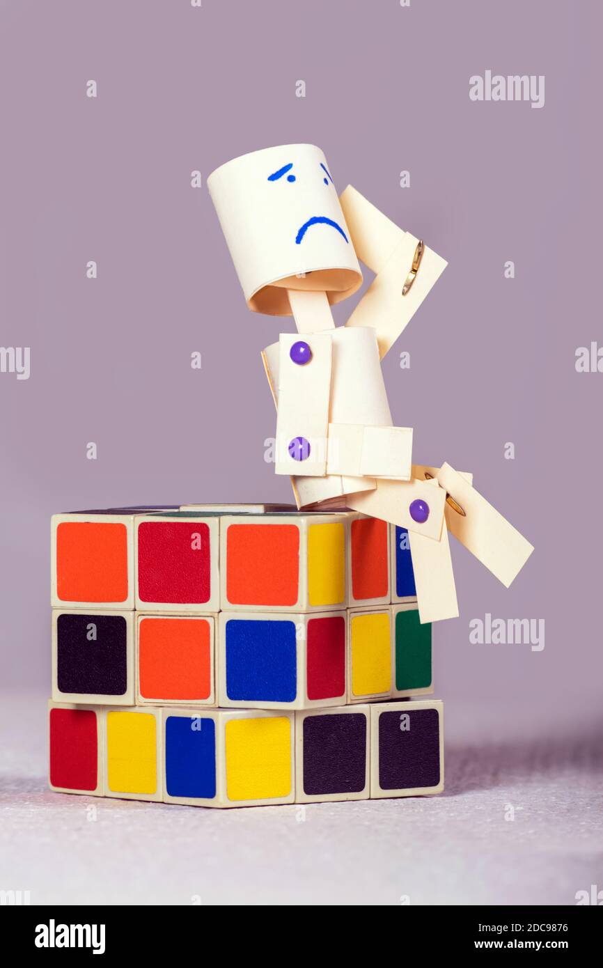 Papierpuppe mit einem müden Ausdruck auf dem Gesicht, sitzt auf einem Standard Rubik Würfel. Stockfoto