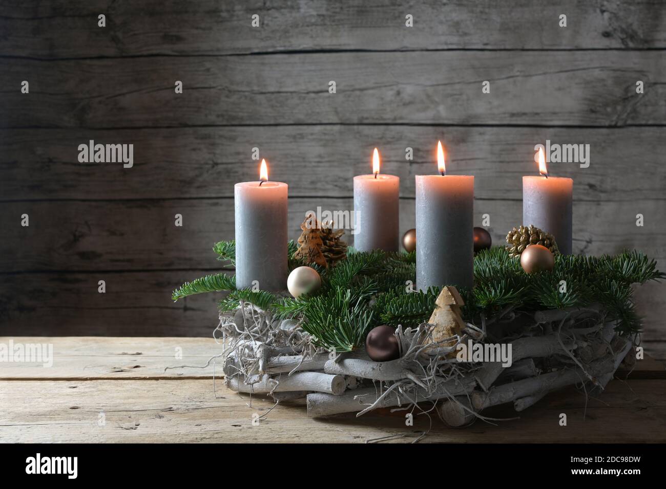Rustikaler Adventskranz aus Holz, Tannenzweigen und Weihnachtsdekoration mit vier brennenden Kerzen gegen eine graue Holzwand mit Kopierraum, ausgesuchter FOC Stockfoto
