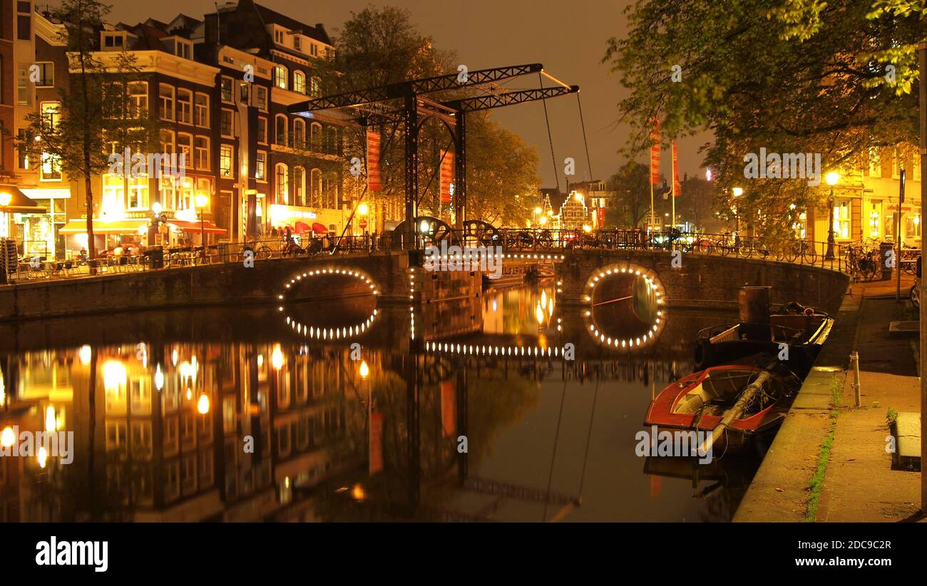 Blick auf die beleuchtete Brücke über den Kanal in Amsterdam bei Nacht Stockfoto