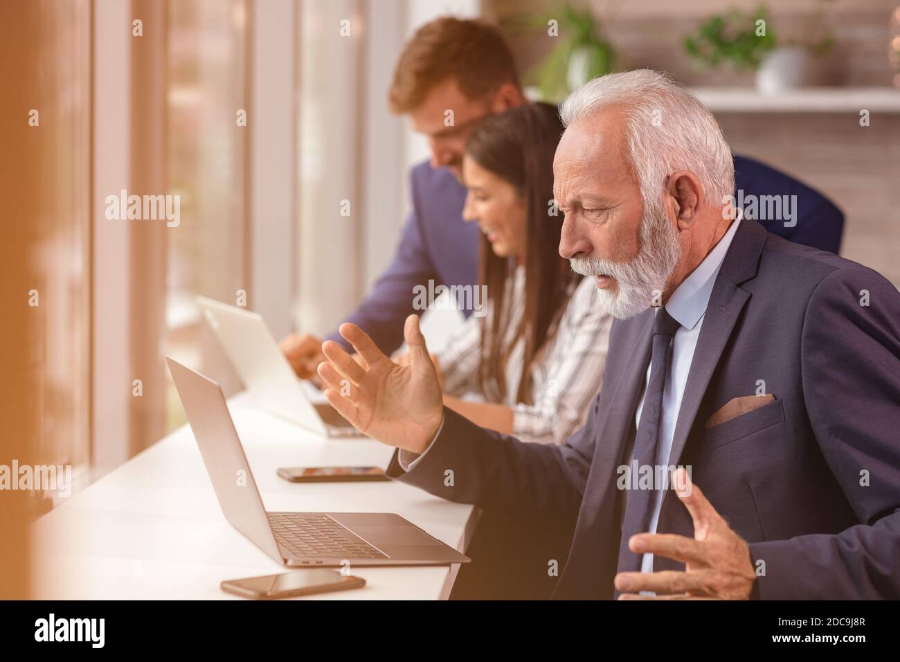 Senior Manager mit einem Laptop mit jungen Kollegen im Hintergrund Stockfoto