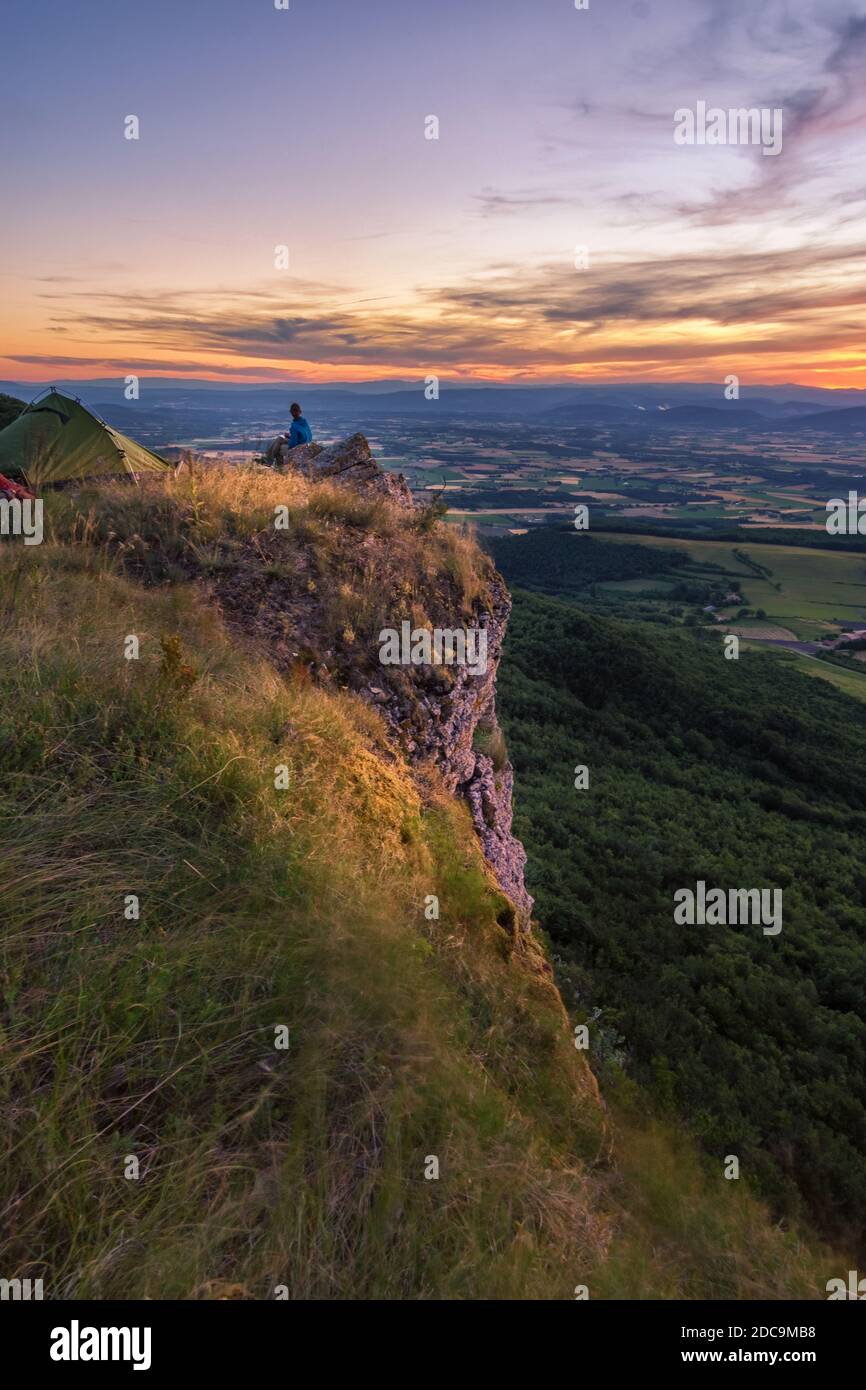 Mann, der auf einer Klippe sitzt und die atemberaubende Landschaft überblickt Bei Sonnenuntergang Stockfoto