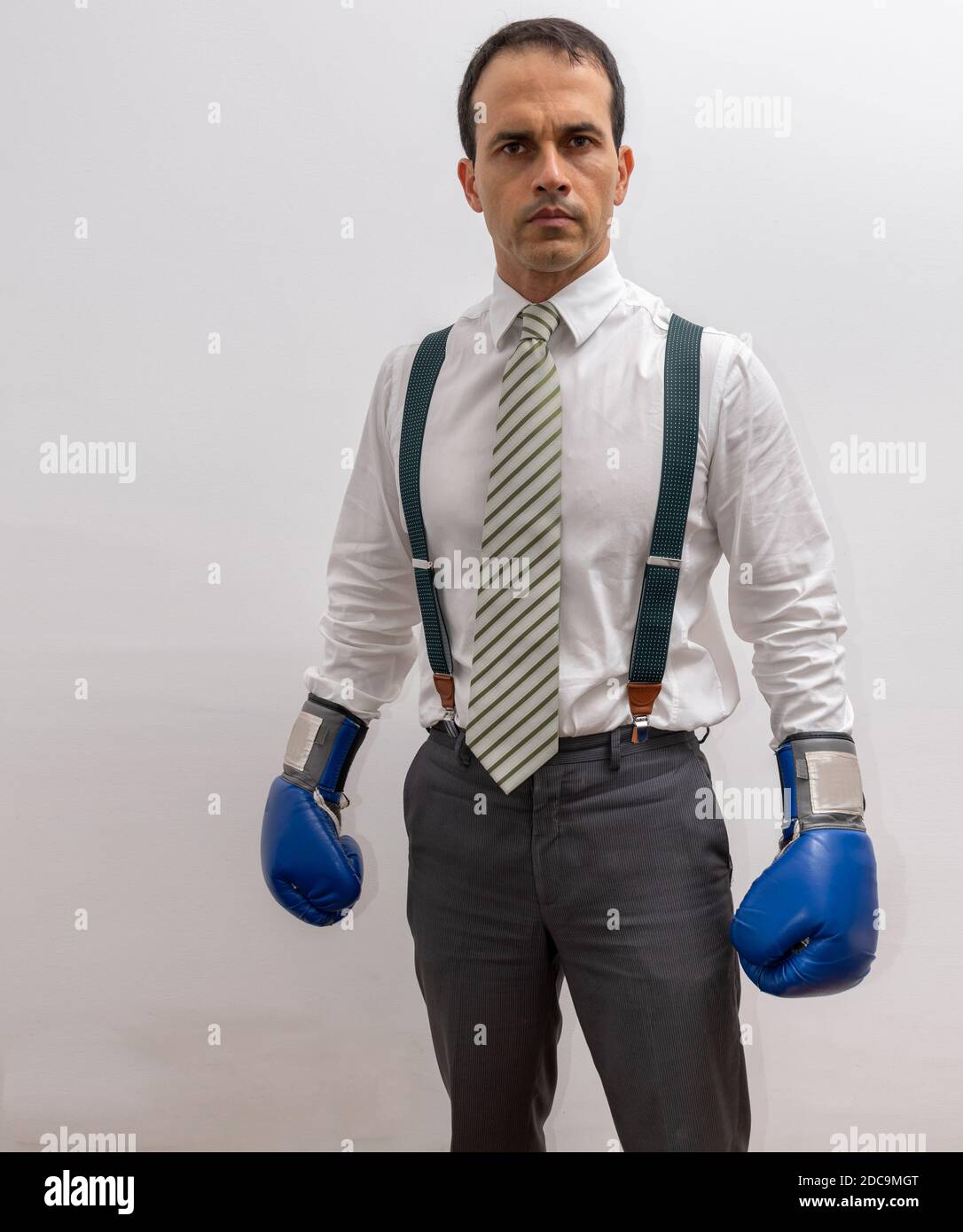 Mann, der mit formeller Kleidung, Hosenträger, Krawatte, Boxhandschuh steht und auf die Kamera starrt. Stockfoto