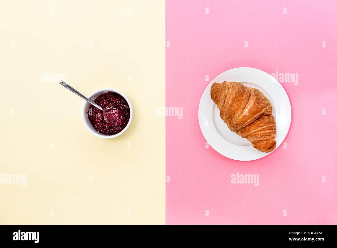 Croissant und eine Kanne Marmelade auf einem gespaltenen rosa und cremefarbenen Hintergrund. Stockfoto