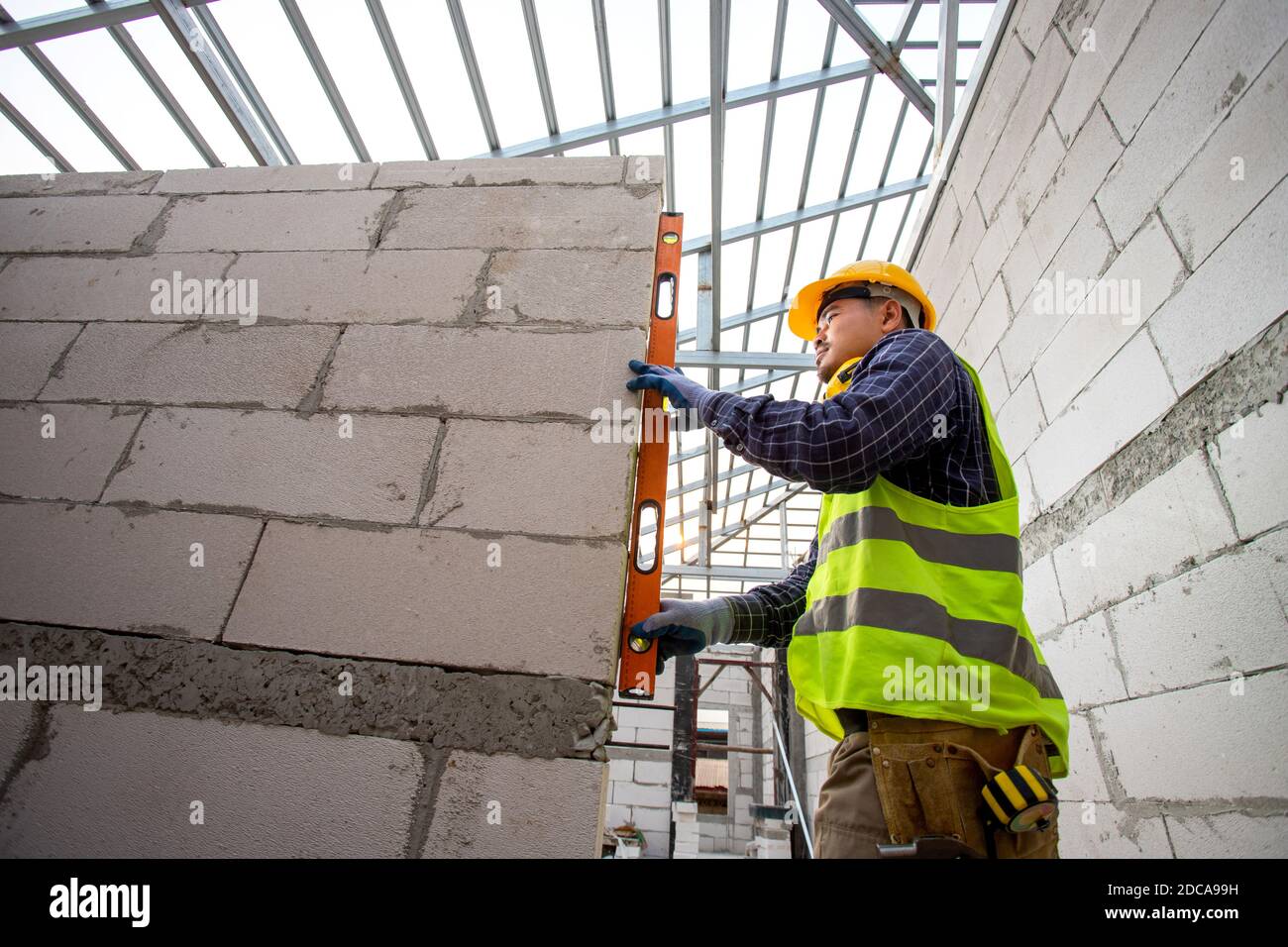 Ein Arbeiter mit einem Wasserpegelmesser, der den Wandbauer mit autoklaviertem, belüfteter Betonklötze misst. Mauerwerk, Ziegel in constru Stockfoto