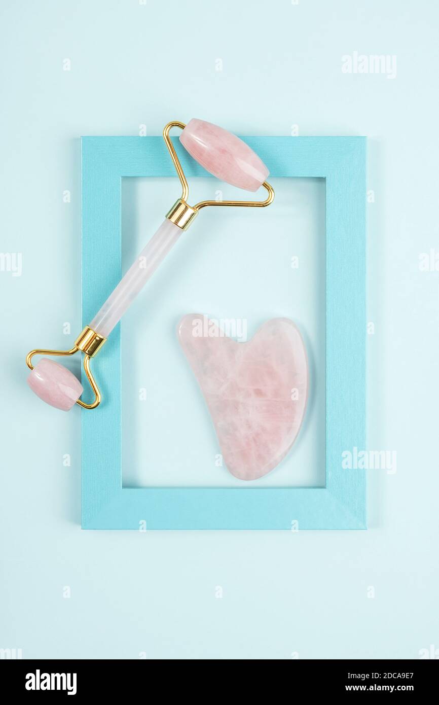 Crystal Rose Quarz Gesichtswalze und Massage-Tool Jade Gua Sha in Rahmen auf blauem Hintergrund. Anti-Age-Gesichtsmassage für natürliches Heben und Toning tr Stockfoto