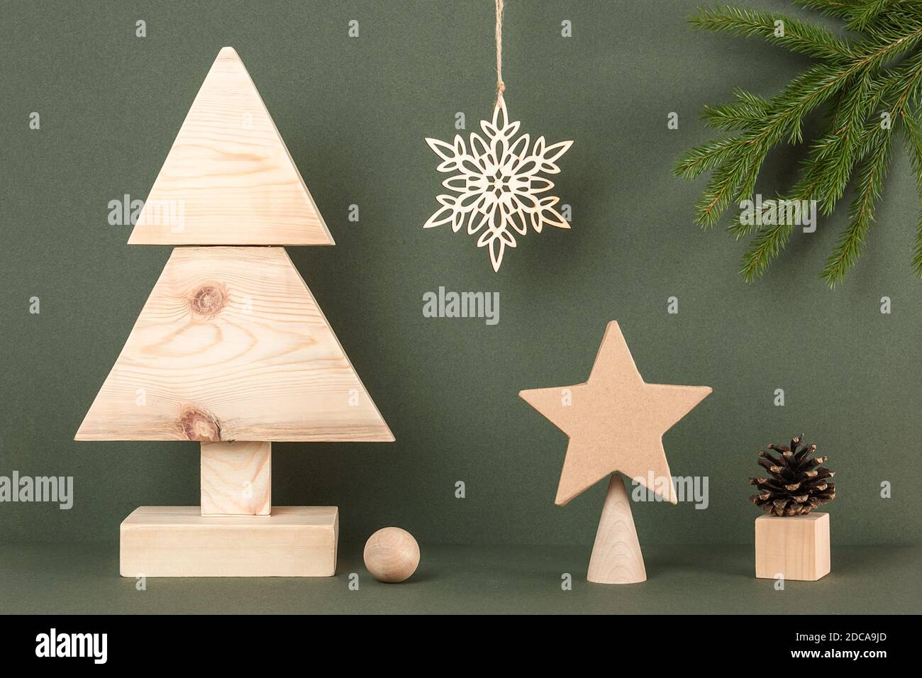 Weihnachten und Neujahr Komposition. Hausgemachter Weihnachtsbaum aus Holz und Weihnachtsdekor auf grünem Hintergrund. Kreatives Konzept Urlaub. Vorderansicht. Stockfoto