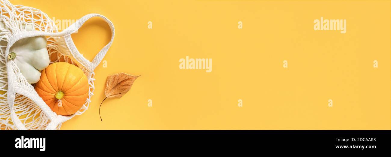 Frisches Erntegemüse Kürbis Kürbis, Pattypan Squash im Einkauf umweltfreundliche Netztasche, Herbstblätter auf gelbem Hintergrund. Konzept Bio-vegeta Stockfoto