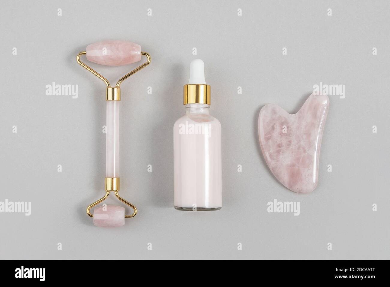 Crystal Rose Quarz Gesichtswalze, Massage-Tool Gua Sha und Anti-Aging-Kollagen, Serum in Glasflasche auf grauem Hintergrund. Gesichtsmassage für natürliche Stockfoto