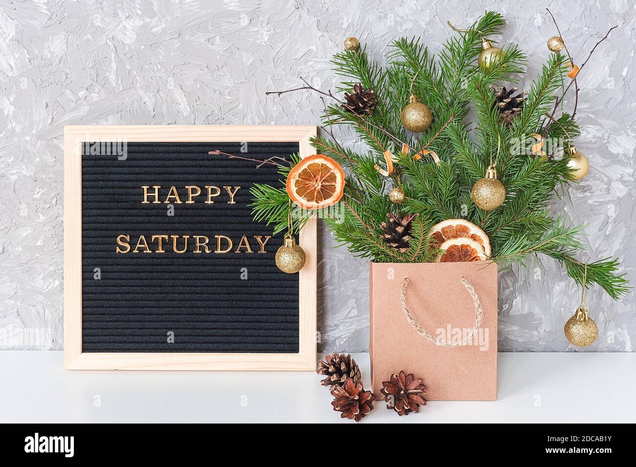 Happy Saturday Text auf schwarzem Briefbrett und festlicher Blumenstrauß von Tannenzweigen mit weihnachtsdekor in Bastelpackung und auf Tisch. Vorlage für Postauto Stockfoto