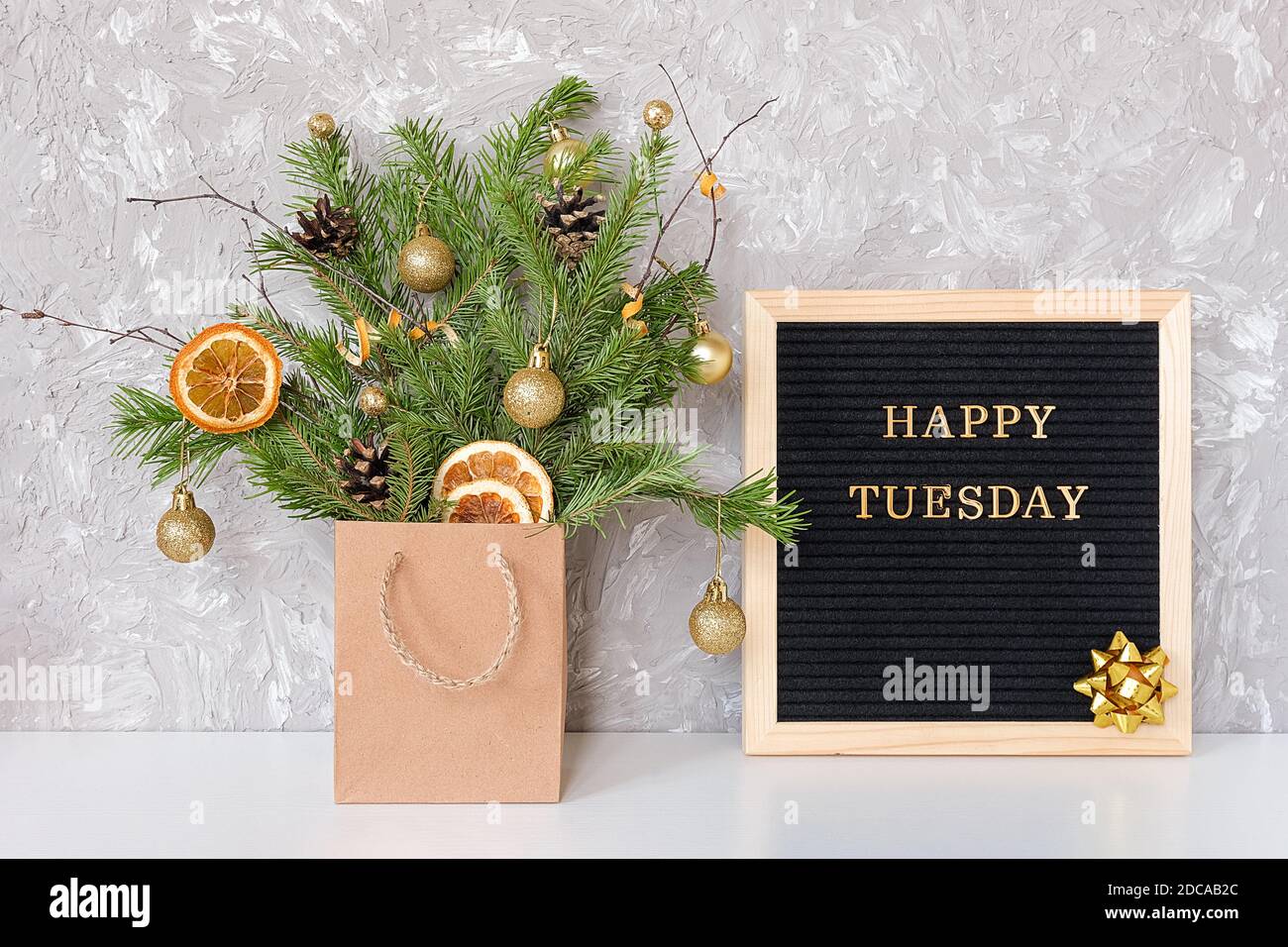 Happy Tuesday Text auf schwarzem Briefbrett und festlicher Blumenstrauß von Tannenzweigen mit weihnachtsdekor in Bastelpackung auf Tisch. Vorlage für Postkarte, gr Stockfoto