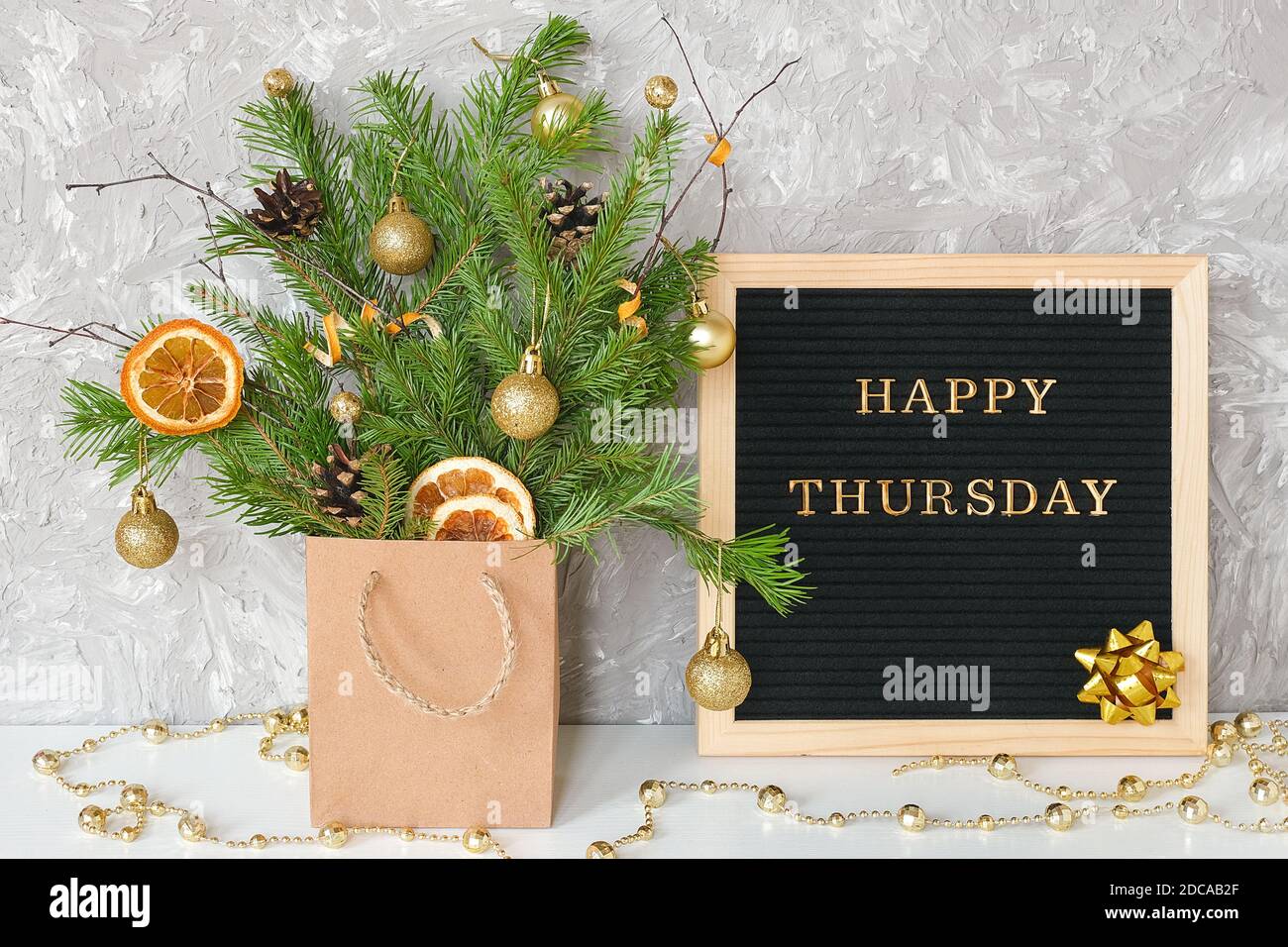 Happy Thursday Text auf schwarzem Briefbrett und festlicher Blumenstrauß von Tannenzweigen mit weihnachtsdekor in Bastelpackung auf Tisch. Vorlage für Postkarte, g Stockfoto
