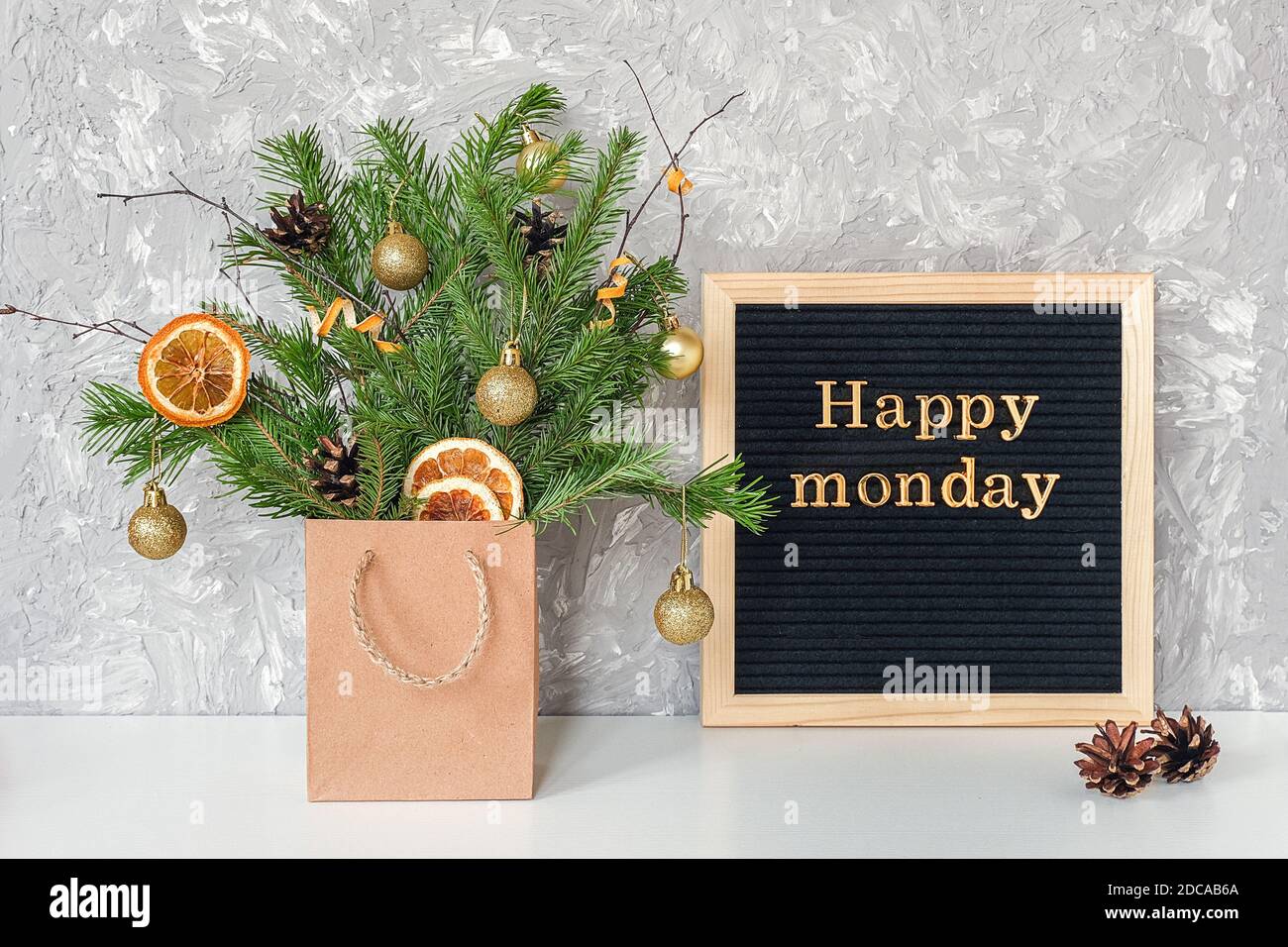 Happy Monday Text auf schwarzem Briefbrett und festlicher Blumenstrauß aus Tannenzweigen mit weihnachtsdekor in Bastelpackung auf Tisch. Vorlage für Postkarte, gre Stockfoto