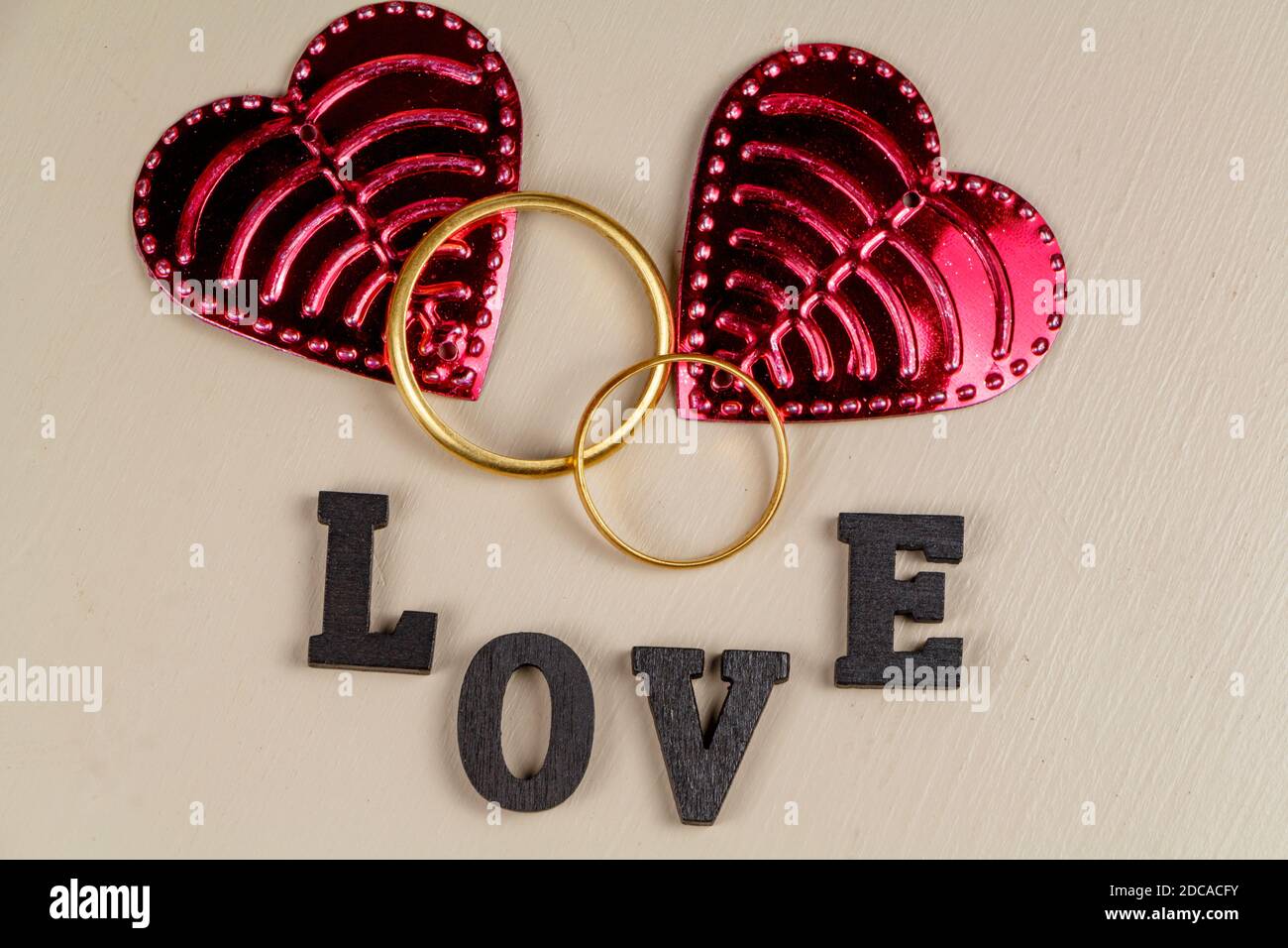 Zwei Eheringe in Gold, zwei rosa Herzen und das Wort Liebe in schwarzem Buchstaben geschrieben Stockfoto