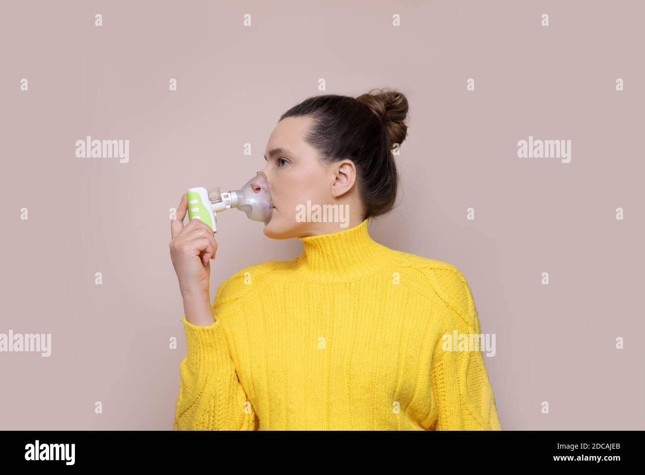 Eine 40-jährige Frau in einem gelben Pullover auf rosa Hintergrund inhaliert die oberen Atemwege, die Lungen mit einem Vernebler. Wegschauen. Studio-Foto Stockfoto