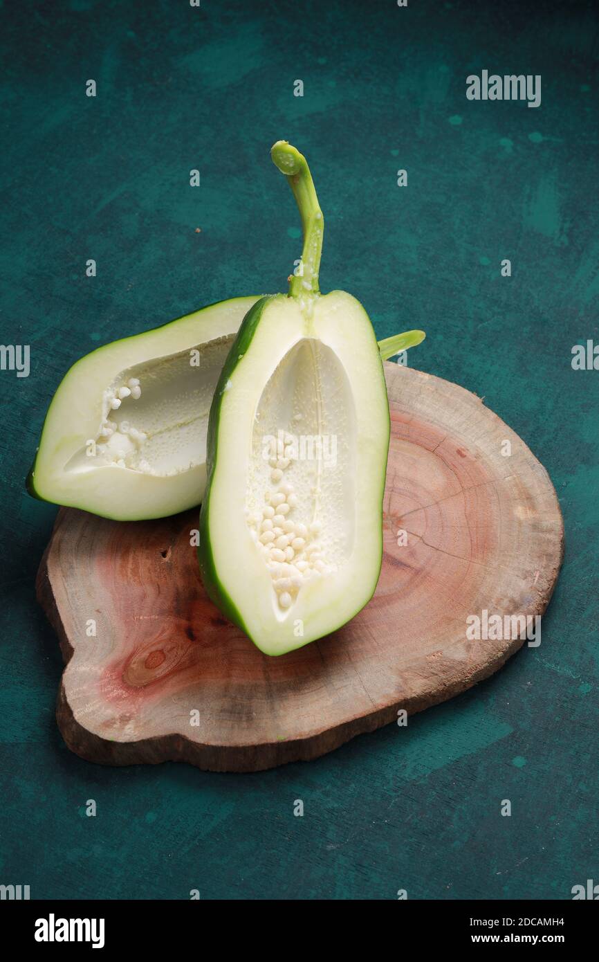 Frische grüne Papaya, aufgeteilt in zwei Stücke und angeordnet auf Ein Holzstück mit dunkelgrünem Hintergrund Stockfoto