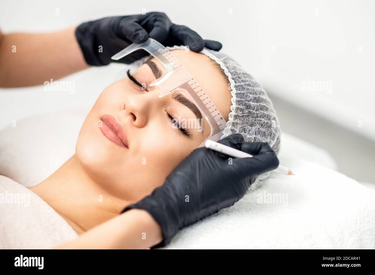 Kosmetikerin misst die Augenbrauen mit Lineal, bevor Augenbrauen tätowiert werden Stockfoto