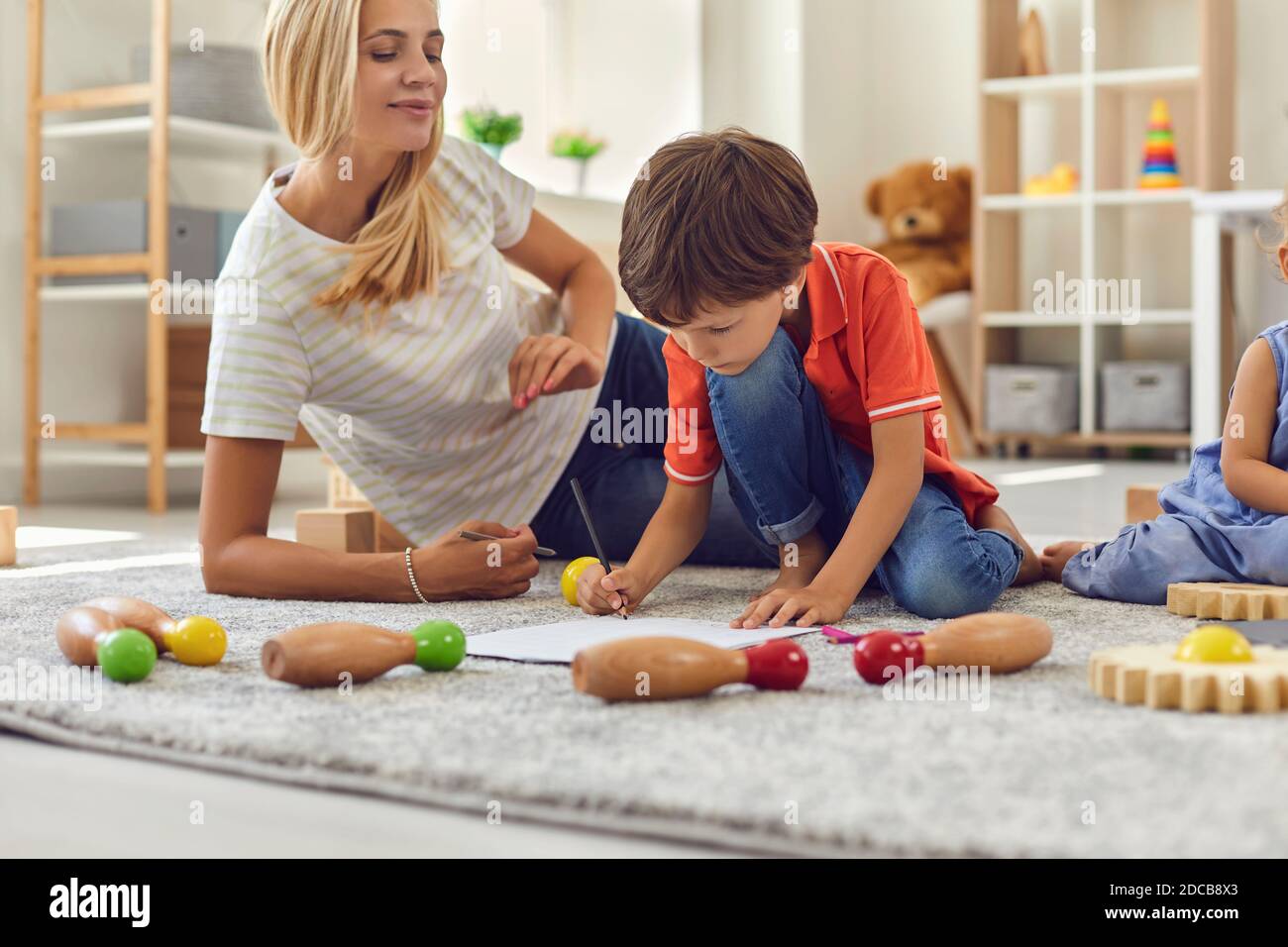 Mutter sitzt mit Kindern auf dem Teppich und zeichnet zusammen Zu Hause Stockfoto