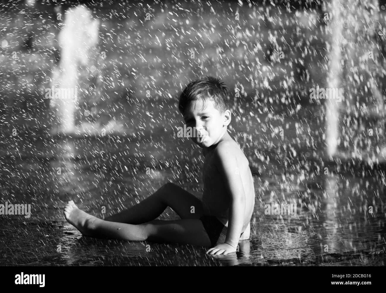 3 Jahre alter glücklicher Junge, der in einem Springbrunnen spielt und an einem heißen Tag die kühlen Wasserströme genießt. Heißer Sommer. Stockfoto