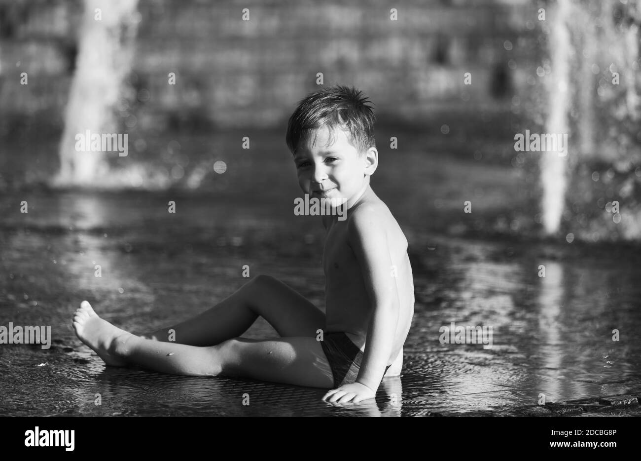 3 Jahre alter glücklicher Junge, der in einem Springbrunnen spielt und an einem heißen Tag die kühlen Wasserströme genießt. Heißer Sommer. Stockfoto